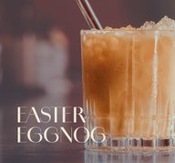 Glas mit ECKES Egg Nog Cocktail auf Eis, mit einem Strohhalm, vor einem unscharfen Barhintergrund