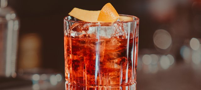 Glas mit ECKES Coffee Negroni Cocktail auf Eis, garniert mit einer Orangenschale, vor einem unscharfen Barhintergrund