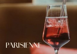 Glas mit ECKES Parisienne Cocktail, in dem ein Spritzer Flüssigkeit aufsteigt, vor einem unscharfen Hintergrund mit der Aufschrift "Parisienne".