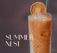 Hohes Glas mit Cocktail Summer Nest und Eiswürfeln, garniert mit einer getrockneten Orangenscheibe.