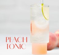 Hohes Glas mit hellrosa Peach Tonic Cocktail, garniert mit einer Limettenscheibe und Eiswürfeln.