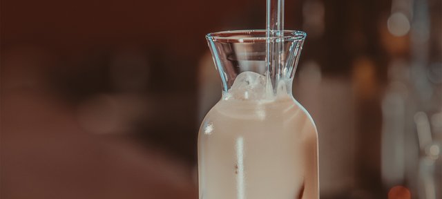 Glasflasche mit ECKES Screaming Cow Cocktail, garniert mit einem Strohhalm, vor einem unscharfen Barhintergrund.