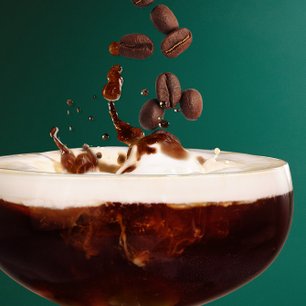 Nahaufnahme eines Kaffeelikörs in einem Cocktailglas mit aufsteigenden Kaffeebohnen