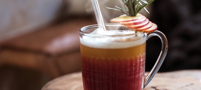 Glas mit ECKES Cherry Punch, garniert mit Apfelscheiben und einem Strohhalm, auf einem Holztisch