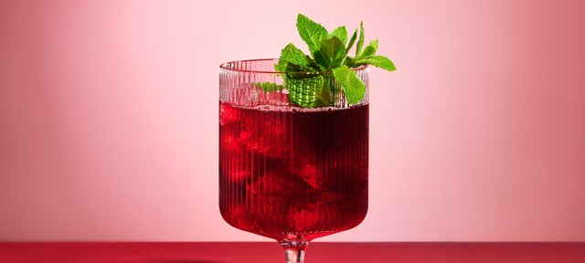 Glas mit ECKES Cherry Smash Cocktail auf Eis, garniert mit frischer Minze, vor einem rosafarbenen Hintergrund.