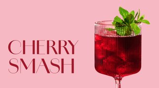 Glas mit ECKES Cherry Smash Cocktail auf Eis, garniert mit frischer Minze, vor einem rosafarbenen Hintergrund