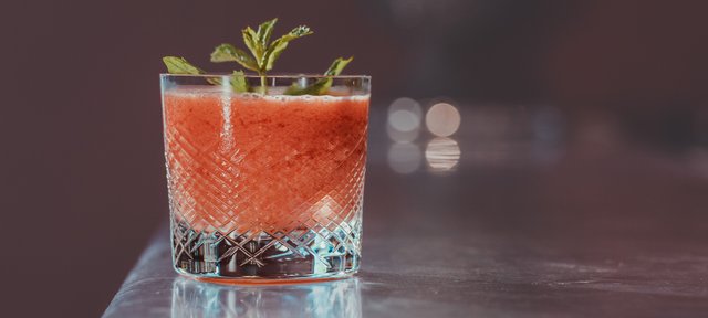 Glas mit ECKES Erdbeer Slush Cocktail, garniert mit frischen Kräutern, auf einer glänzenden Oberfläche