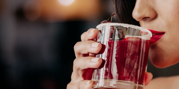 Eine Frau mit roten Lippen trinkt einen Cherry Smash Cocktail aus einem Glas mit Zuckerrand.