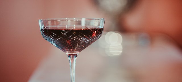 Glas mit ECKES Vanderbilt Cocktail, vor einem unscharfen, warm beleuchteten Hintergrund.