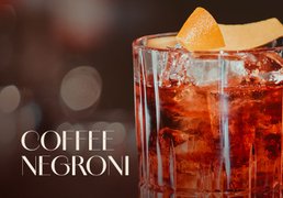 Tumbler-Glas mit rotem ECKES Coffee Negroni Cocktail, garniert mit einer Orangenzeste und Eiswürfeln.