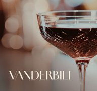 Glas mit ECKES Vanderbilt Cocktail, vor einem unscharfen, warm beleuchteten Hintergrund mit der Aufschrift "Vanderbilt"