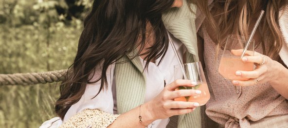 Zwei Frauen halten Cocktails in der Hand und stehen nah beieinander im Freien.