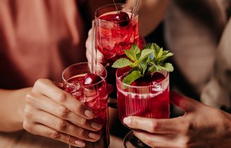 Drei Personen stoßen mit Gläsern mit ECKES Edelkirsch Longdrinks an, garniert mit Kirschen und Minzblättern