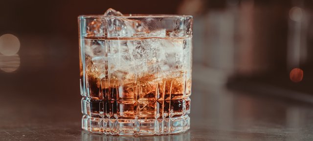 Glas mit ECKES Black Russian Cocktail auf Eis, vor einem unscharfen Barhintergrund.