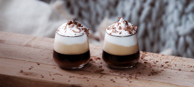 Zwei Gläser mit ECKES Black Forest Espresso Drink, garniert mit Sahne und Schokoladenstreuseln, auf einem Holztisch