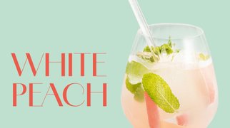 Glas mit hellrosa White Peach Cocktail, garniert mit Minzblättern und Eiswürfeln.