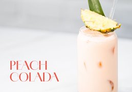 Glas mit rosa Peach Colada Cocktail, garniert mit einer Ananasscheibe und einem Ananasblatt.