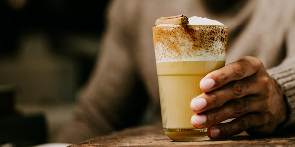  Eine Hand hält ein Glas mit einem Eierlikör-Drink, garniert mit Sahne und Zimt.