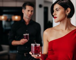 Eine Frau im roten Kleid hält einen ECKES Edelkirsch Longdrink, ebenso wie ein Mann im Hintergrund. 