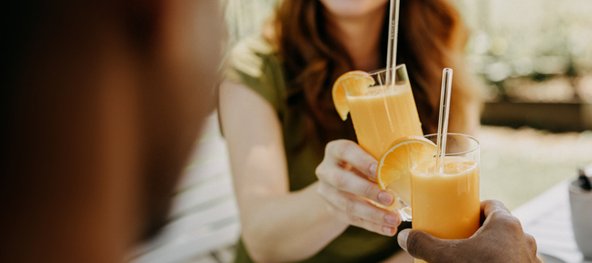 Zwei Personen stoßen mit Eierlikör-Drinks in hohen Gläsern an, garniert mit Orangenscheiben und Strohhalmen.