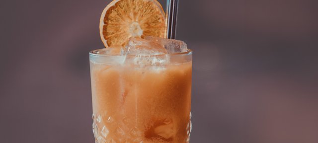 Glas mit ECKES Summer Nest Cocktail auf Eis, garniert mit einer getrockneten Orangenscheibe und einem Strohhalm.