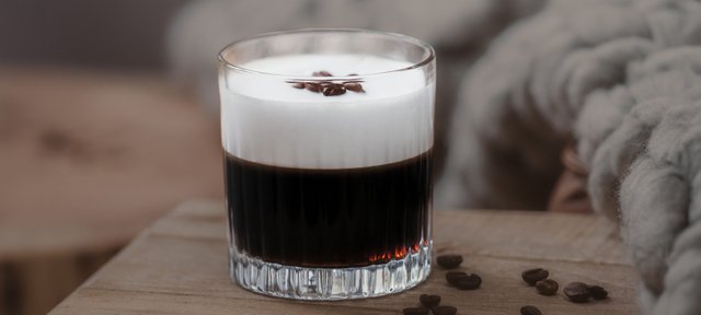 Glas mit ECKES Irish Coffee, garniert mit Sahne und Kaffeebohnen, auf einem Holztisch vor einem unscharfen, gemütlichen Hintergrund.