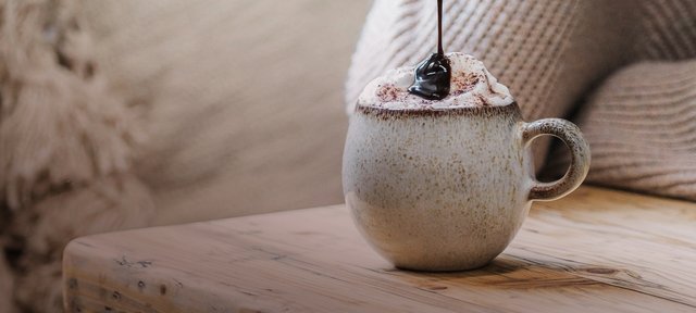 Tasse mit ECKES Chocolate Cherry, garniert mit Sahne und einer Kirsche, auf einem Holztisch vor einem gemütlichen Hintergrund.